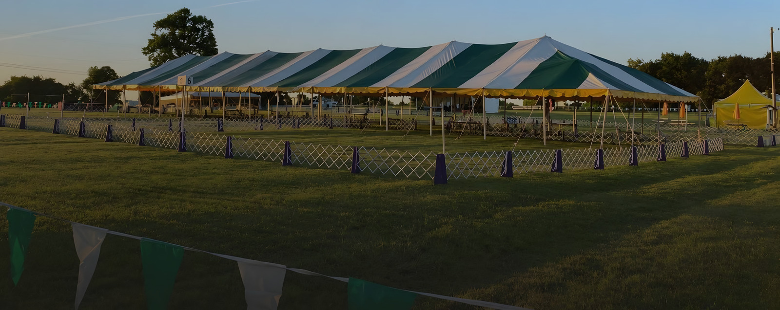 Green and white striped show tent over the rings at a dog show, early evening.